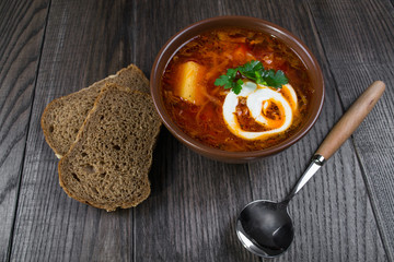 Tomato soup . Traditional  Ukrainian beetroot and tomato soup - borsch in clay pot with sour cream, herbs and bread on dark wooden background.