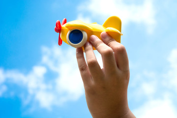 child hand holding yellow toy plane flying in the sky