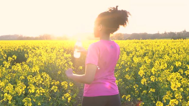 4K video clip of beautiful healthy mixed race African American girl teenager female young woman running or jogging with a bottle of water in field of yellow flowers