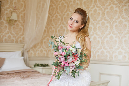Pretty young Bride.blonde-haired woman with wedding hair-style with a long tail. Boudoir morning of the bride. Looking on her bouquet