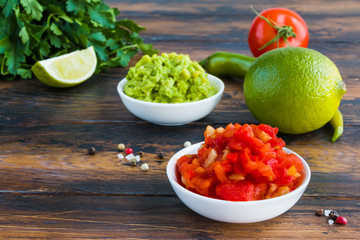 Traditional Mexican sauces salsa and guacamole in small white bowls and fresh vegetables on the...