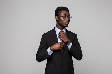 Afro amerocan business man in suit make his tie on grey background