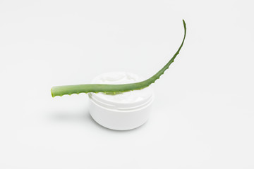 Close-up view of organic cream in container and aloe vera plant isolated on white