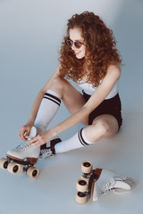 High angle view of hipster girl in sunglasses wearing roller skates sitting isolated on grey