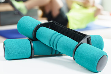 Fitness at home concept, a pair of green dumbbells in the foreground and man doing sit ups on exercise mat in the background in fitness in living room.