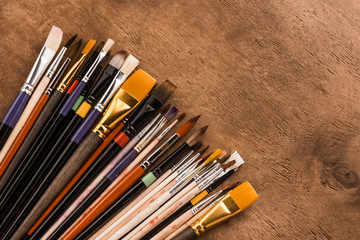 Close-up top view of various paintbrushes collection on brown wooden table