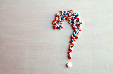 question mark made of capsules on  white wood, space for text