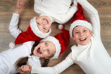 three kids in Santa hats lying on wooden background, having fun and happy emotions, winter holiday concept