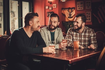 Cheerful old friends having fun and drinking draft beer in pub.