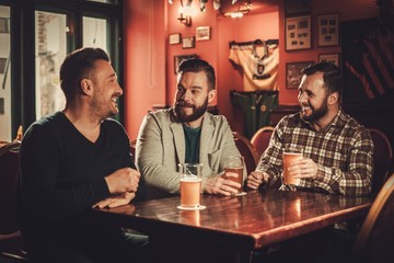 Cheerful old friends having fun and drinking draft beer in pub.