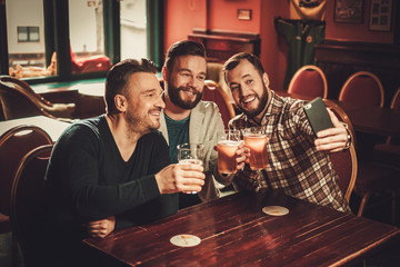 Cheerful old friends having fun and drinking draft beer in pub.
