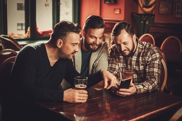 Cheerful old friends having fun and drinking draft beer in pub.