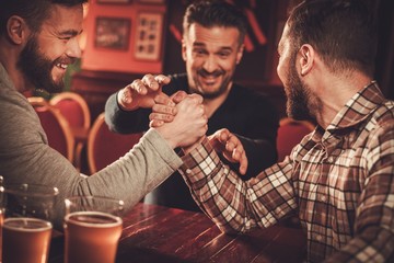 Cheerful old friends having arm wrestling challenge in a pub.