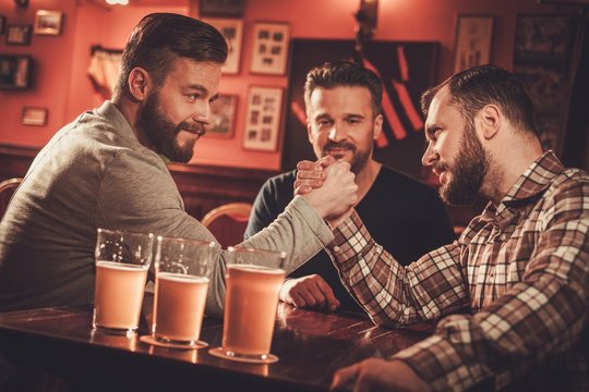 Cheerful old friends having arm wrestling challenge in a pub.