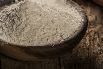 Flour in a wooden bowl, paper bag and spoon. Top view, space for text.