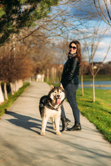 A girl is walking with a dog along the embankment. Beautiful Husky dog. The river. Spring.