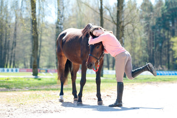 Young cheerful teenage girl owner hugging her favorite horse