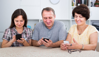 Smiling mature parents with daughter sitting with phones