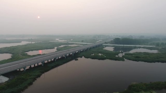 Aerial View. The picturesque landscape with river, highway bridge, trees and field with Incredible sun. Morning Fog.