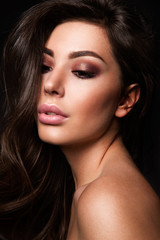 Fototapeta premium Glamour portrait of beautiful girl model with makeup and romantic wavy hairstyle. Fashion shiny highlighter on skin, sexy gloss lips make-up and dark eyebrows.