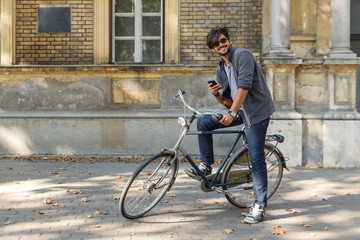 Young handsome guy with a bicycle on street looking at mobile phone.