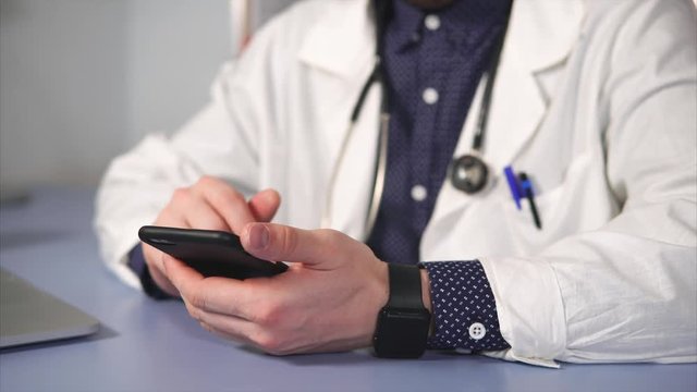 close up shot of the therapist hands, who uses the phone to find the composition of medicines. A man in a white robe holds a mobile phone and uses a touch screen