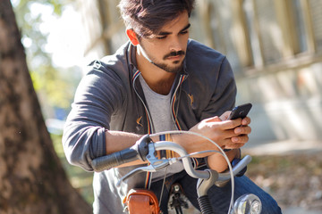 Young handsome guy with a bicycle on street looking at mobile phone.