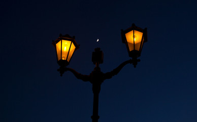 Fototapeta na wymiar A young month above a lamp post with two lighted lanterns against the background of the night sky