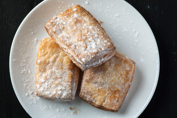 Puff pastries in a white plate on a black wooden table, top view