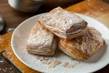 Puff pastry cookies in a white plate on a wooden table, closeup shot