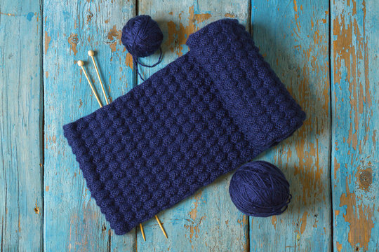 Two coils of wool, knitting needles and a blue knitted scarf