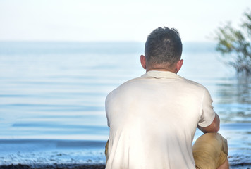 A young guy sits and stares into the distance on the seashore