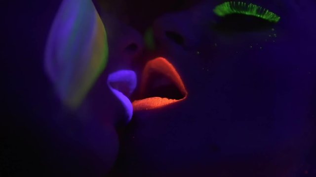 Beautiful woman inhaling hookah in fluorescent clothing under UV black light and exhaling to face of another woman