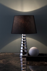 elegante lampada da tavolo accesa su piano in marmo, vicina a sfera in pietra.