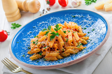 Traditional Italian meal made of penne pasta and arrabiata sauce with parsley on a white table. Delicious healthy Mediterranean food on a blue rustic plate.