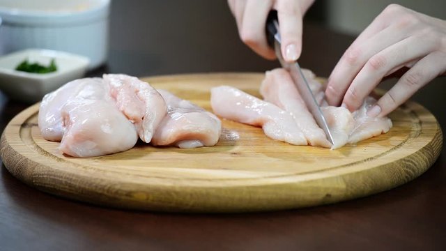 Food preparing, cooking concept. Female hands cutting slicing raw chicken meat breast on board