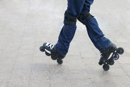 Young man wearing roller skates and protective knee pads riding on a city tile
