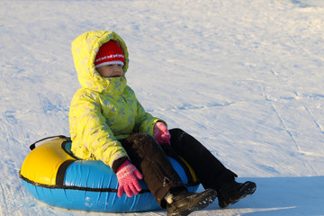 Fototapeta na wymiar Girl sits on snowtube and looks away at sunny and frosty winter day