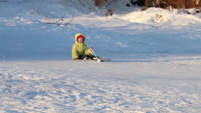Girl skier slides down from hill and falls at winter day, two unrecognizable children are on hill