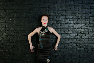 Young woman in black dress with makeup poses in studio near black wall