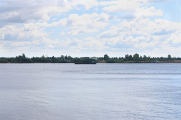 Naklejka premium Cargo ship sails on river with green coastline at summer sunny day