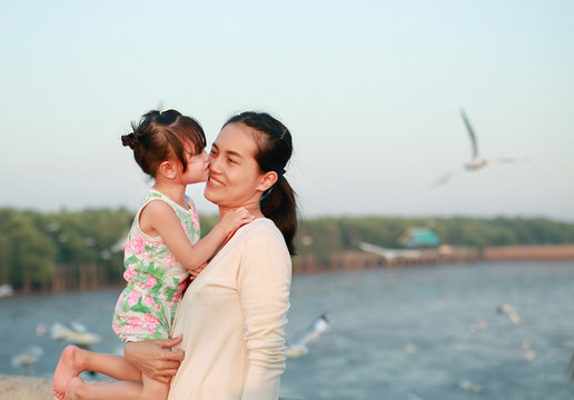 Portrait of Mother and daughter cuddling, Beautiful little girl hugging her mother against lagoon with flying bird.