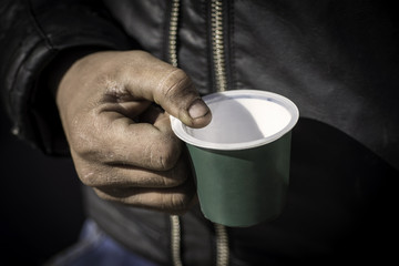 Dirty Beggar Hand Holding Plastic Cup. Poor Man Begging for Money on the Street Close Up.