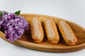 Eclairs on white background on wooden plate with lilac