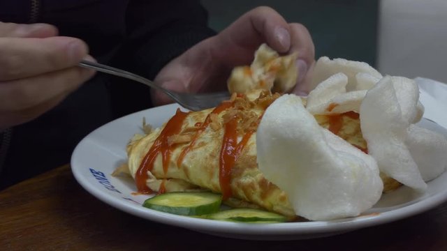 Man eating Pattaya fried rice and shredded chicken covered with omelette or omelet, Nasi goreng pattaya in Malaysian cafe