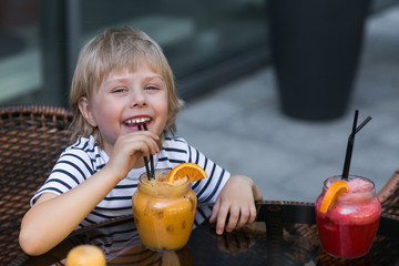 Fototapeta premium Very cute little boy in the cafe drinking fresh lemonade. Emotional cheerful kid or child outdoors wearing sunglasses and smiling. Adorable child with cocktail