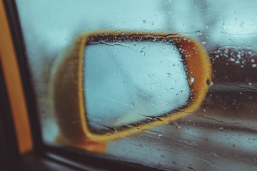 Yellow car rear view mirror with road reflection, rainy weather. photo depicting raindrops on a...