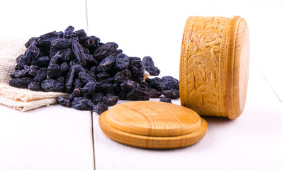 Blue raisins scattered on burlap in a wooden cup on a white wooden table.