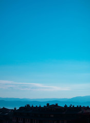 Photo depicting a beautiful European mountain landscape with city chalet roofs silhouettes in front. European alpine mountains with snow peaks on a clean blue sky background.
