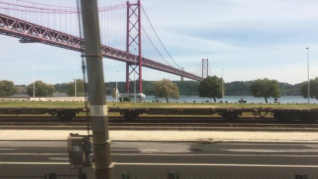 Train Travel In Lisbon Window View of Famous Bridge In Tagus River. POV Train ride through city of Lisbon on a beautiful sunny day